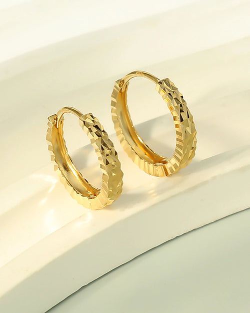 Diamond cut gold hoop earrings on white display surface